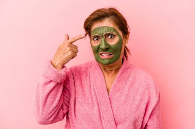 Middle age caucasian woman wearing a facial mask isolated on pink background showing a disappointment gesture with forefinger.