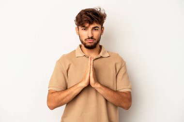 Genç melez adam gri arka planda izole edilmiş dua ediyor, bağlılık gösteriyor, dindar biri ilahi ilham arıyor..