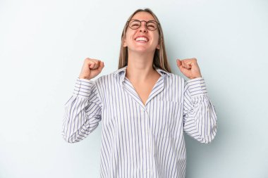 Mavi arka planda izole edilmiş genç beyaz kadın zaferi, tutkuyu ve coşkuyu kutluyor, mutlu bir ifade..