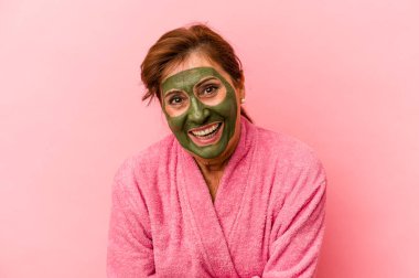 Middle age caucasian woman wearing a facial mask isolated on pink background laughing and having fun.