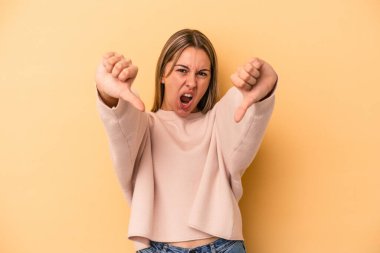 Sarı arka planda izole edilmiş genç beyaz kadın baş parmağını aşağı gösteriyor ve hoşlanmadığını ifade ediyor..