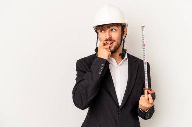 Miğfer takan ve taksimetre tutan genç mimar gri arka planda rahat bir şekilde fotokopi odasına bakan bir şeyi düşünüyor..