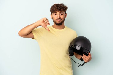 Mavi arka planda izole edilmiş motosiklet kaskı tutan melez genç adam hoşlanmadığı bir jest gösteriyor. Anlaşmazlık konsepti.
