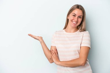 Mavi arka planda izole edilmiş genç beyaz kadın bir avuç içinde fotokopi alanı ve belinde bir el daha gösteriyor..