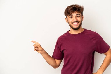 Gri arka planda izole edilmiş genç melez adam işaret parmağıyla işaret ederek neşeyle gülümsüyor..