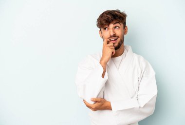 Mavi arka planda karate yapan genç melez bir adam rahatlamış fotokopi alanına bakan bir şey düşünüyor..