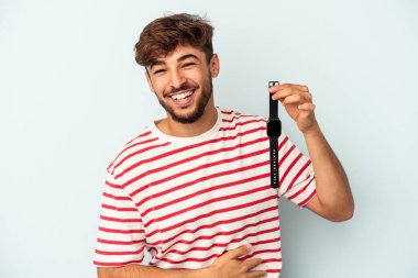 Kol saati tutan genç melez adam mavi arka planda izole edilmiş gülüyor ve eğleniyor..