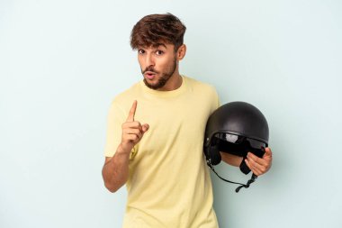 Mavi arka planda izole edilmiş motosiklet kaskı tutan genç melez adamın bir fikri var, ilham verici bir kavram..