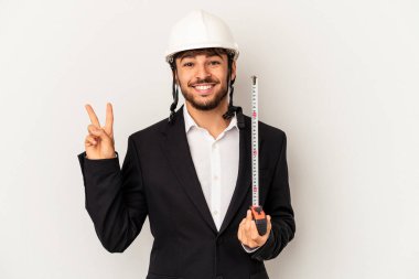 Miğfer takan ve taksimetre tutan genç mimar gri arka planda neşeli ve kaygısız bir barış sembolünü parmaklarıyla gösteriyor..