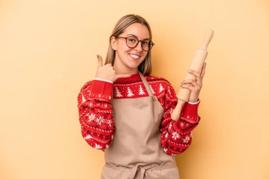 Genç fırıncı kadın Noel için kurabiye yapıyor. Sarı arka planda izole edilmiş. Cep telefonu hareketini parmaklarıyla gösteriyor..