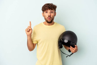 Mavi arka planda izole edilmiş motosiklet kaskı tutan genç melez adamın harika bir fikri var, yaratıcılık kavramı..