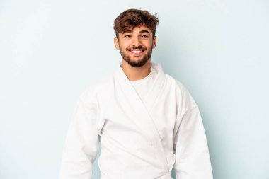 Mavi arka planda karate yapan genç melez adam mutlu, güler yüzlü ve neşeli..