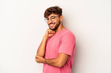 Genç melez adam gri arka planda izole edilmiş mutlu ve kendinden emin gülümsüyor, elleriyle çenesine dokunuyor..