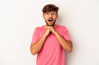 Genç melez adam gri arka planda izole edilmiş şans için dua ediyor, şaşırmış ve ağzı açık bir şekilde önüne bakıyor..