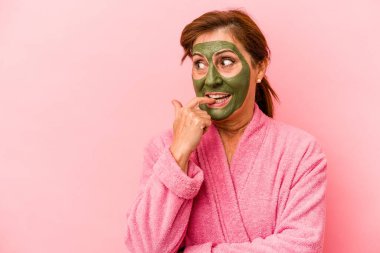 Middle age caucasian woman wearing a facial mask isolated on pink background relaxed thinking about something looking at a copy space.