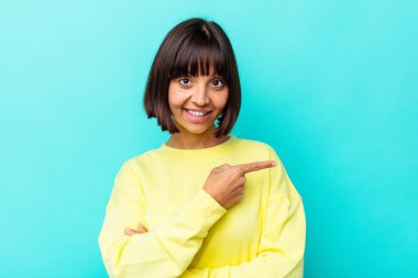 Mavi arka planda izole edilmiş genç, melez bir kadın gülümsüyor ve boş alanda bir şeyler gösteriyor..