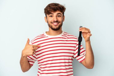 Mavi arka planda izole edilmiş bir kol saati tutan genç melez adam bir gömlek fotokopi alanını işaret ediyor, gururlu ve kendinden emin.