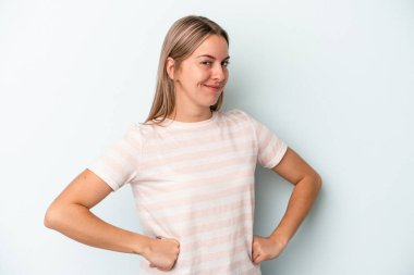 Mavi arka planda izole edilmiş genç beyaz kadın hoşnutsuzca kaşlarını çatmış, kollarını kavuşturmuş..