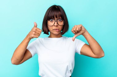 Mavi arka planda izole edilmiş genç melez kadın baş parmağını kaldırıyor, zor seçim konsepti.