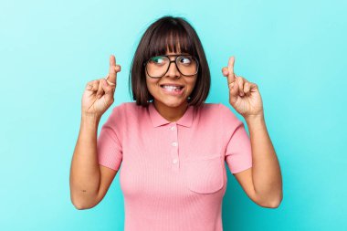 Mavi arka planda izole edilmiş genç melez kadın şans getirsin diye dua ediyor.