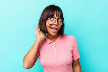 Mavi arka planda izole edilmiş genç melez kadın bir dedikoduyu dinlemeye çalışıyor..