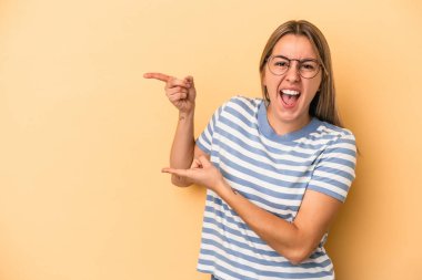 Sarı arka planda izole edilmiş genç beyaz kadın işaret parmağıyla işaret ederek heyecanlanıyor..