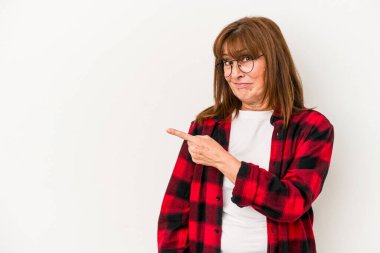 Beyaz arka planda izole edilmiş orta yaşlı beyaz bir kadın gülümsüyor ve boş alanda bir şeyler gösteriyor..