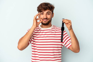 Kol saati tutan melez genç bir adam mavi arka planda izole edilmiş ve dudakları dudaklarında bir sır saklıyor..