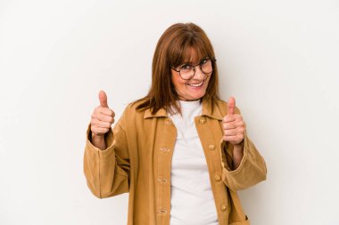 Beyaz arka planda soyutlanmış orta yaşlı beyaz bir kadın. Baş parmağını kaldırıyor, gülümsüyor ve kendinden emin..