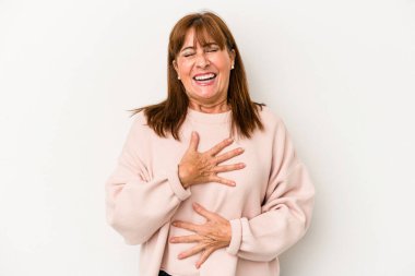 Beyaz arka planda izole edilmiş orta yaşlı beyaz kadın mutlu bir şekilde gülüyor ve ellerini karnının üstünde tutarak eğleniyor..