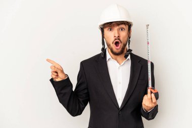 Miğfer takan ve taksimetre tutan genç bir mimar gri arka planda izole edilmiş, yan tarafı işaret ediyor.