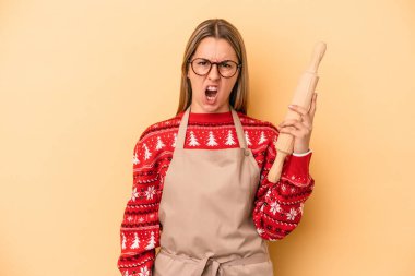 Genç fırıncı kadın Noel için kurabiye yapıyor sarı arka planda izole edilmiş çok kızgın ve agresif çığlıklar atıyor..