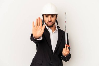 Mimar, miğfer takıyor ve taksimetre takıyor. Gri arka planda izole halde duruyor. Elini uzatıp dur işareti gösteriyor..