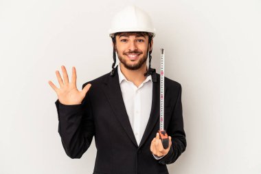 Miğfer takan ve taksimetre tutan genç mimar gri arka planda izole edilmiş gülümseyen beş numarayı parmaklarıyla gülümsüyor..