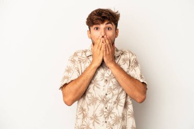 Genç melez adam gri arka planda izole edilmiş şok olmuş, ağzı ellerle kaplanmış, yeni bir şey keşfetmeye hevesli..