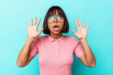 Genç melez kadın mavi arka planda izole edilmiş gökyüzüne haykırıyor, yukarı bakıyor, hayal kırıklığına uğramış..