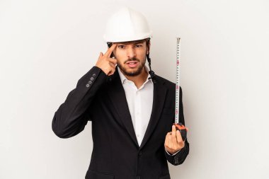 Miğfer takan ve gri arka planda taksimetre tutan genç mimar işaret parmağıyla yaptığı hayal kırıklığı jestini gösteriyor..