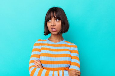 Mavi arka planda izole edilmiş genç, melez bir kadın kameraya alaycı bir ifadeyle bakıyor..