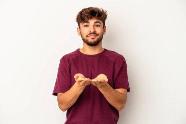 Genç melez adam gri arka planda izole edilmiş. Elinde avuç içi olan bir şeyle kameraya sunuyor..