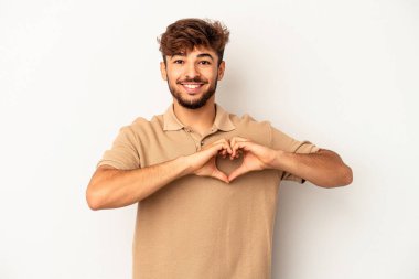 Genç melez adam gri arka planda izole edilmiş gülümsüyor ve elleriyle kalp şeklini gösteriyor..