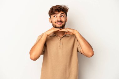 Gri arka planda izole genç melez adam ellerini çenesinin altında tutuyor, mutlu bir şekilde yana bakıyor..