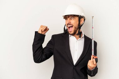 Miğfer takan ve taksimetre tutan genç mimar gri arka planda, zafer kazandıktan sonra yumruğunu kaldırıyor..