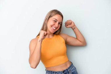 Mavi arka planda izole edilmiş genç beyaz kadın özel bir günü kutluyor, atlıyor ve enerjiyle kollarını kaldırıyor..