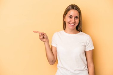 Sarı arka planda izole edilmiş genç beyaz kadın işaret parmağıyla işaret ederek gülümsüyor..