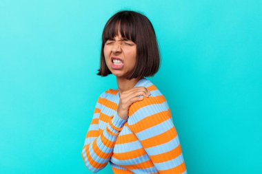 Mavi arka planda izole edilmiş, omuz ağrısı çeken genç bir ırk kadını..