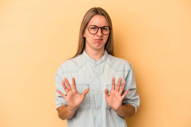 Sarı arka planda izole edilmiş genç beyaz kadın tiksinti belirtisi gösteren birini reddediyor..
