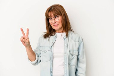 Beyaz arka planda izole edilmiş orta yaşlı beyaz kadın neşeli ve kaygısız parmakları olan bir barış sembolü gösteriyor..