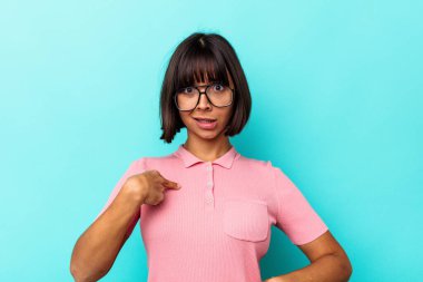Mavi arka planda izole edilmiş genç bir ırk kadını parmağını göstererek şaşırdı, geniş bir gülümsemeyle..