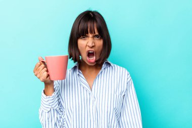 Mavi arka planda pembe kupa tutan genç melez kadın çok sinirli ve agresif çığlıklar atıyor..