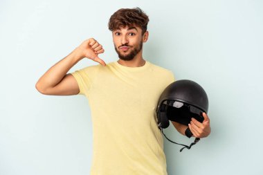 Mavi arka planda izole edilmiş motosiklet kaskı tutan genç melez adam gururlu ve kendinden emin hissediyor, örnek olarak..